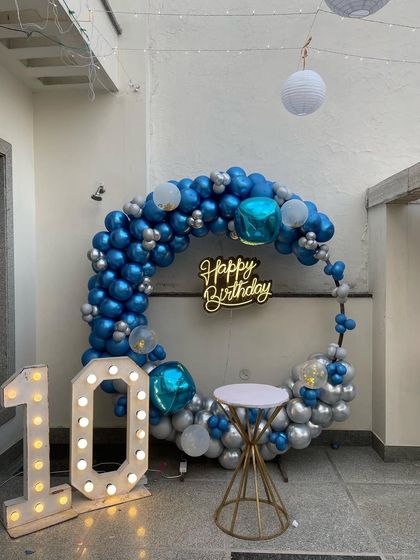 A 10th birthday celebration on a terrace, featuring a blue and silver balloon ring, a neon sign, and a '10' marquee number.