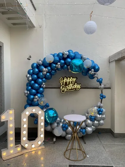 A stylish 10th birthday setup on a home terrace, featuring a blue and silver balloon ring and a light-up marquee number.