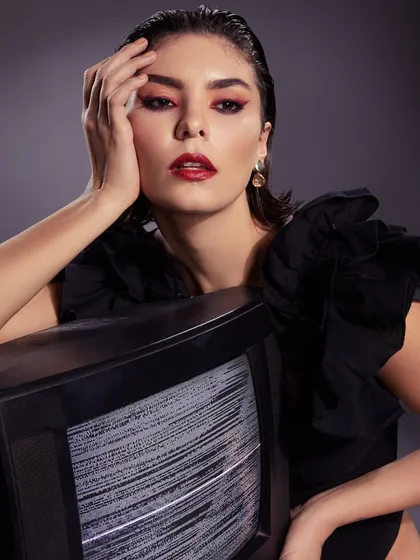 A retro-inspired glam look with a red lip and winged liner, creatively styled with a vintage television set.