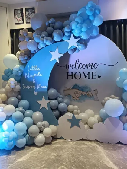 A "Welcome Home Little Miracle & Super Mom" setup with a celestial moon and stars theme. The blue, white, and beige balloons create a calming and dreamy look, celebrating both the new baby and the new mother.