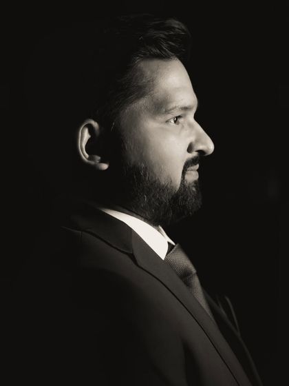 A dramatic, low-key profile portrait of the groom. The black and white treatment emphasizes the light and shadow, creating a powerful and classic image.