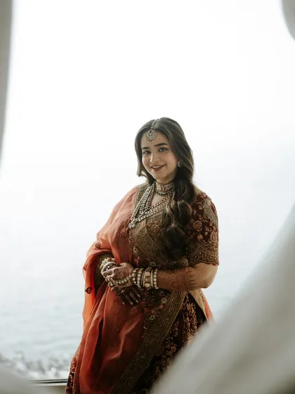 A beautiful bridal portrait taken through a window frame. The soft, natural light and the serene ocean view create a peaceful and elegant image.