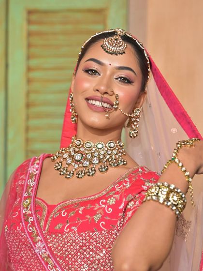 A close-up of a smiling model in a pink lehenga, highlighting the stunning kundan choker and nath. I provide complete jewellery sets for rent.
