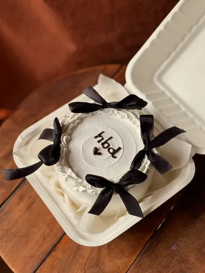 Sometimes, simple is the most beautiful. This minimalist bento cake features clean white frosting, a simple "hbd" message, and is elegantly decorated with four delicate black satin bows for a chic, Pinterest-inspired look.