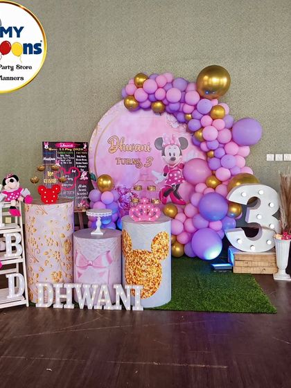 A pretty Minnie Mouse-themed third birthday. The setup features a purple and pink balloon arch, themed plinths, and a large light-up number '3'.