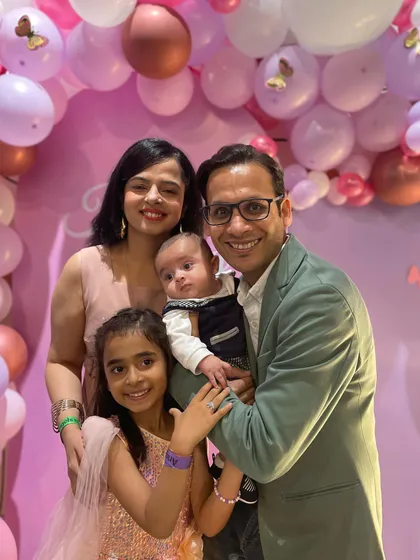 A beautiful family of four posing in front of a pink butterfly-themed balloon backdrop. It's a perfect snapshot of a happy family celebrating a special day together.