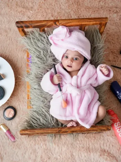 Another angle of the adorable newborn spa day theme, this time from above, showing the baby with eyes open. The setup includes a tiny wooden bed, makeup brushes, and palettes for a playful and unique photoshoot.