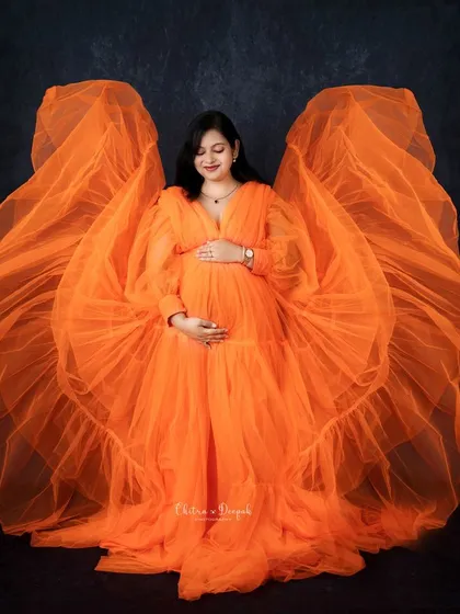 A burst of vibrant orange. This flowing gown with wing-like sleeves creates a dramatic and unforgettable look for a bold and artistic maternity session.