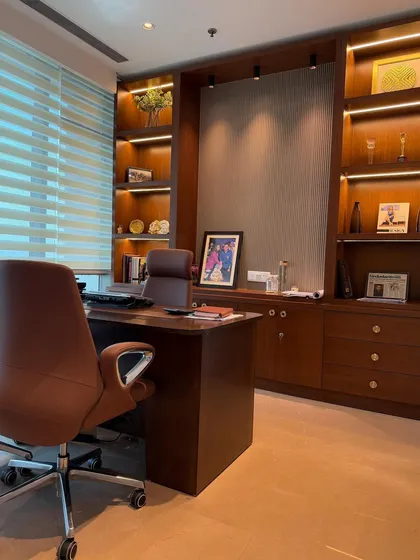We design office spaces that are both functional and inspiring. This executive cabin features custom-built wooden shelving with integrated backlighting, an ergonomic chair, and a clean layout to create a productive and aesthetically pleasing work environment.