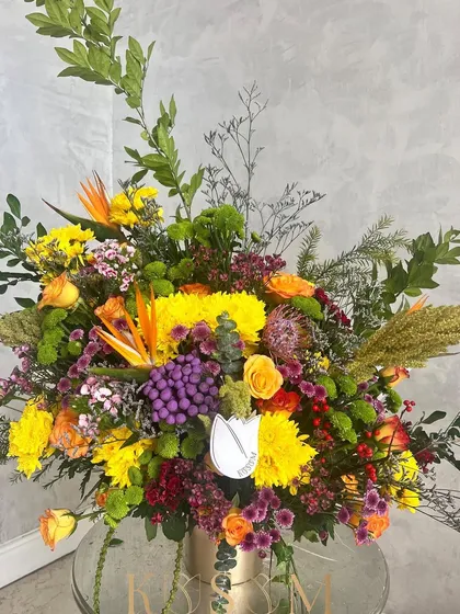 Confetti in a vase. This vibrant and expressive arrangement is perfect for Mother's Day, combining Albiflora, Ilex berries, Pincushions, Roses, and Birds of Paradise for a joyful and poised look.
