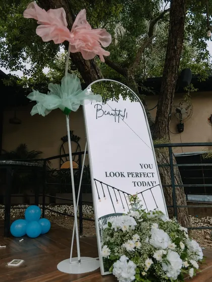 An elegant welcome sign for a Dior-inspired baby shower. The arched mirror with custom vinyl lettering, accented with a lush arrangement of white flowers, creates a sophisticated first impression for guests as they arrive.