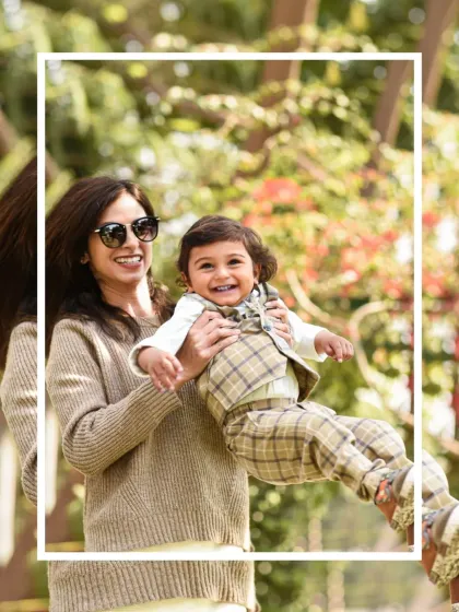 A mother joyfully lifts her laughing son in the air during their outdoor family photoshoot. The natural setting allows for spontaneous and playful interactions.