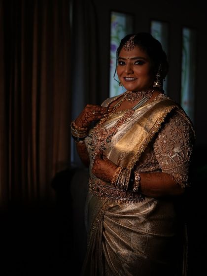 A portrait of a bride in a dimly lit room. The light catches the gold of her saree, creating a beautiful and dramatic effect.