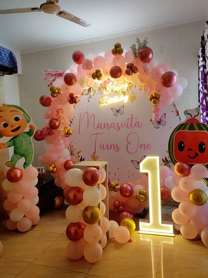 A sweet Cocomelon and butterfly theme for a first birthday. This home setup includes character cutouts, a personalized backdrop, a pink balloon arch, and a light-up number '1'.
