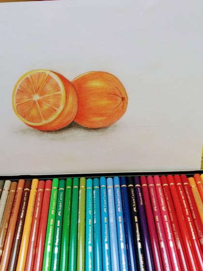 A set of color pencils next to a finished drawing of oranges, showing the tools of our trade.