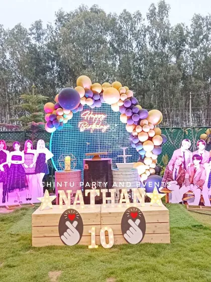 An elaborate outdoor K-Pop themed birthday party setup in Bangalore. This large-scale decoration includes a custom stage, light-up marquee letters, and life-sized cutouts of BTS and Blackpink band members.
