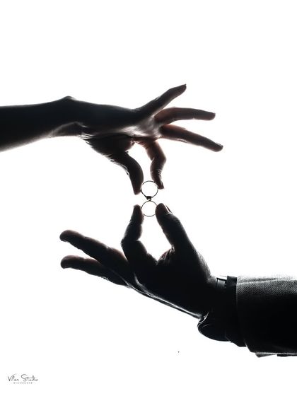 A creative silhouette of the couple's hands exchanging rings. This image uses negative space and shadow to create a powerful and artistic representation of the wedding commitment.