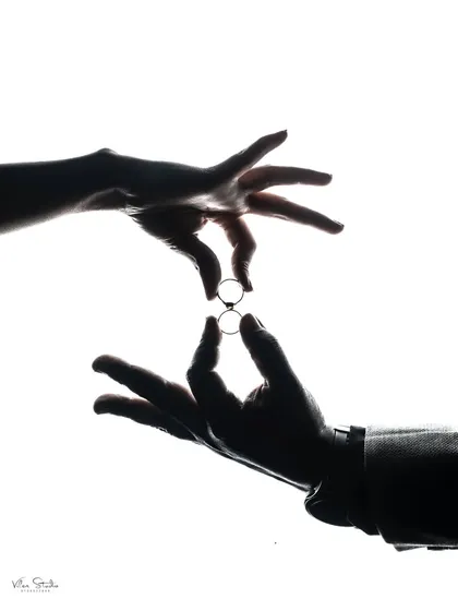 A close-up silhouette shot of the couple's hands exchanging rings. This is a powerful, symbolic image that focuses on the act of commitment.