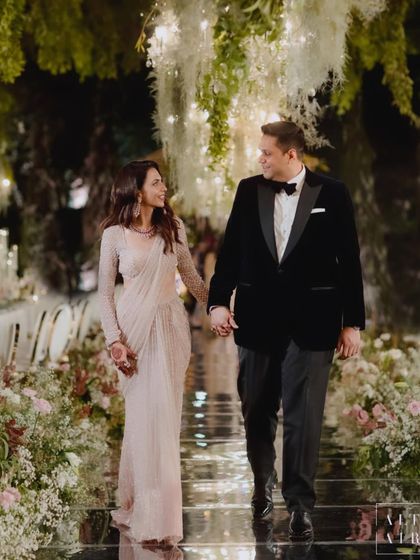The couple walks hand-in-hand through an enchanting English garden-themed reception. The mirrored aisle reflects the cascading floral installations, creating a soulful journey of love.