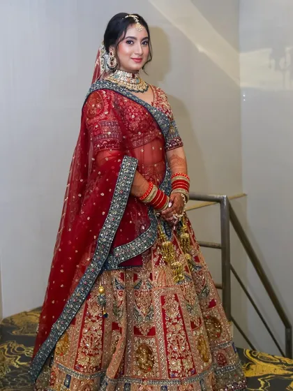 A full-length shot of the bride on a staircase, showcasing her magnificent red and gold lehenga.