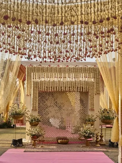 The entrance to the wedding, with a pathway flanked by pink consoles holding vintage vases of tuberoses, all under a canopy of hanging florals.