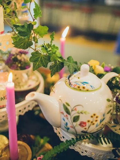A close-up of the curated tablescape, featuring a floral teapot, delicate teacups filled with flowers, and soft candlelight. We layered textures and details to make the setting feel rich and enchanting.