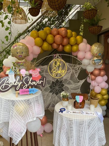 A charming and rustic 'Oh Baby' baby shower setup. This decoration features a macrame backdrop, a multi-colored balloon arch, and themed props for a gender-neutral celebration.