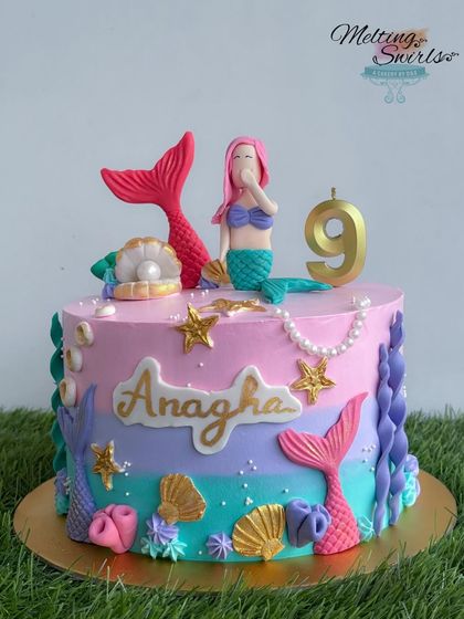 This single-tier mermaid cake is perfect for a smaller celebration. It features beautiful pastel ombre frosting and is adorned with all handmade fondant accents like a mermaid, shells, and stars.