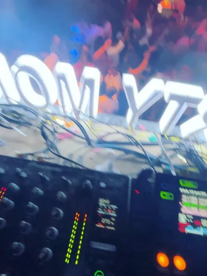 A close up of the DJ decks with the glowing "Party Monkeyz" sign and a confetti filled dance floor in the background.