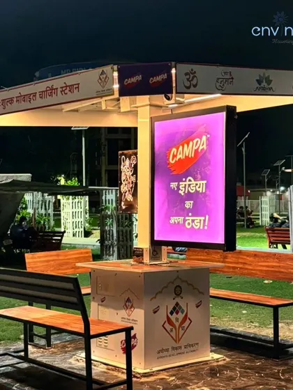 A full view of the solar hut near Hanuman Garhi, showcasing the comfortable bench seating and the bright digital advertising screen. It serves as both a public utility and a communication platform.