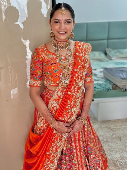 The bride looks stunning in her orange lehenga, her hair styled in a chic and elegant floral bun.