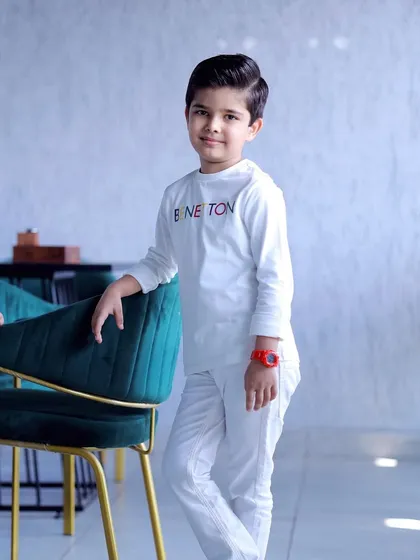 A full-length shot of the birthday boy posing with a modern chair, showing off his complete outfit from head to toe.