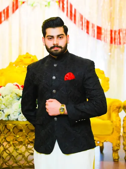 A classic groom's look with a black textured bandhgala and a pop of red from the pocket square. The gold watch adds a touch of luxury.