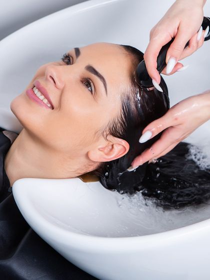 The simple pleasure of a luxurious hair wash. A client relaxes and smiles, enjoying the first step of her rejuvenating hair care ritual.