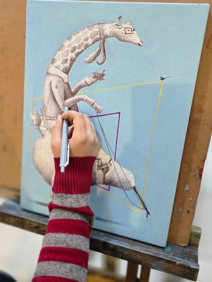 A close-up of a young artist's hand as she carefully adds details to her surreal giraffe drawing with a ballpoint pen.