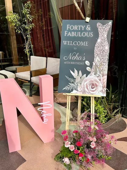 A personalized welcome area for the "Forty & Fabulous" celebration. It features a custom welcome sign on an easel, a large pink initial "N" for the birthday girl, and a beautiful fresh floral arrangement.