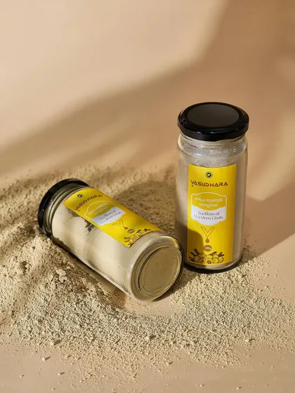 Vasudhara face pack jars styled on a bed of powder. This shot communicates the product's natural, earthy form and texture.