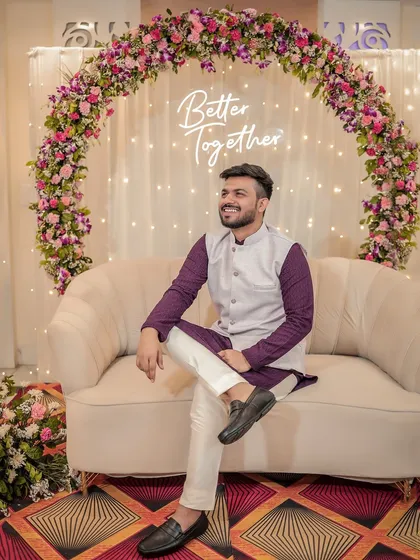 A portrait of the groom at his Roka ceremony, seated in front of a "Better Together" neon sign.
