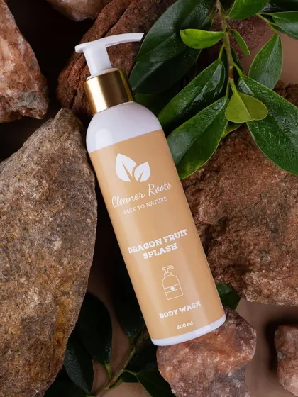 A product shot of Cleaner Roots' Dragon Fruit Splash body wash, nestled among natural rocks. The composition gives the product a rugged, elemental, and organic feel.