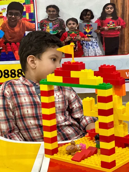A close-up shot of a child's hands as he carefully builds a tall, colorful structure.