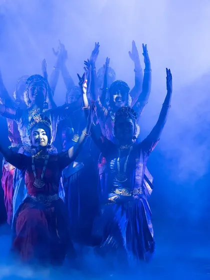 A powerful group pose from "KRISHNA", with dancers' arms raised in unison amidst a mystical blue haze. This captures the unity and devotion of the gopis.