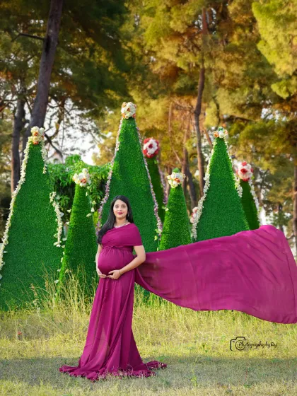 A solo portrait in a wine-colored fabric wrap, showcasing the beautiful baby bump against a backdrop of our unique cone-shaped green props.