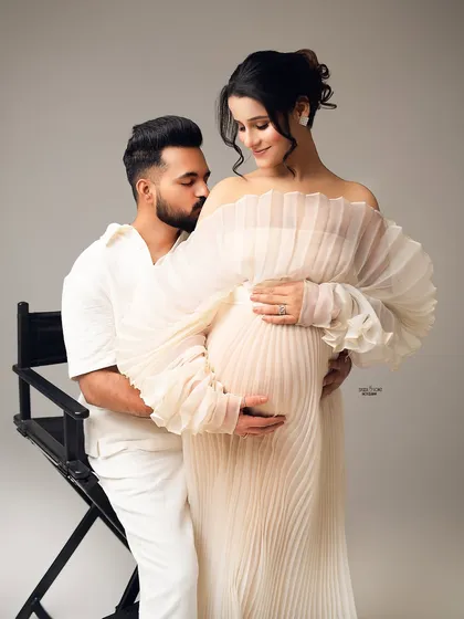 Angelic and serene. This all-white studio maternity photo features a stunning pleated gown with ruffled sleeves, creating a soft, ethereal look that is both gentle and glamorous.
