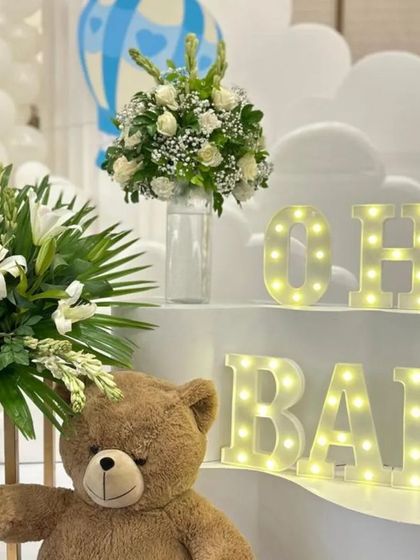 A close-up of the 'Oh Baby' marquee letters, a popular choice for baby showers. The soft glow adds a magical touch, especially when paired with a cute teddy bear and fresh flowers.