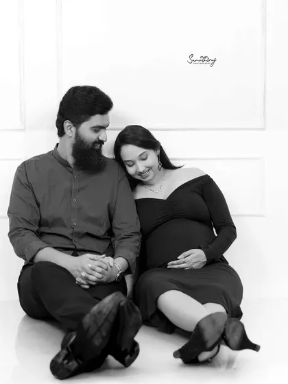 A tender black and white portrait of a couple seated on the floor. The wife rests her head on her husband's shoulder, creating a quiet, intimate, and emotional moment.
