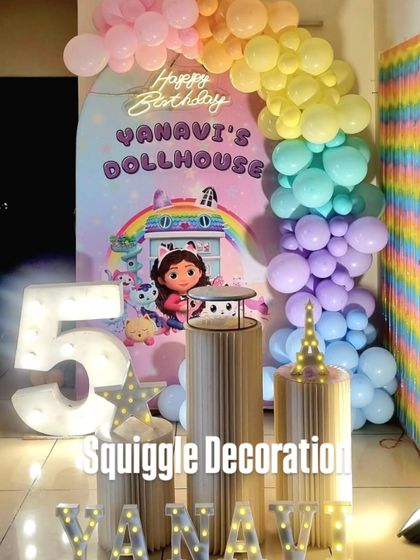 A colorful 'Dollhouse' themed 5th birthday party. The setup includes a custom backdrop, a rainbow balloon column, and a large marquee number '5'.