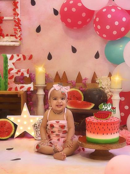A perfect portrait before the smashing begins! She looks so sweet in her strawberry dress, sitting beside her watermelon cake in this colourful studio setup.