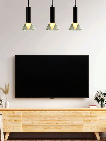 A trio of modern industrial-style pendants hangs over a media console. This linear arrangement provides excellent task lighting while bringing a new dawn of artful, luxury lighting to the space.