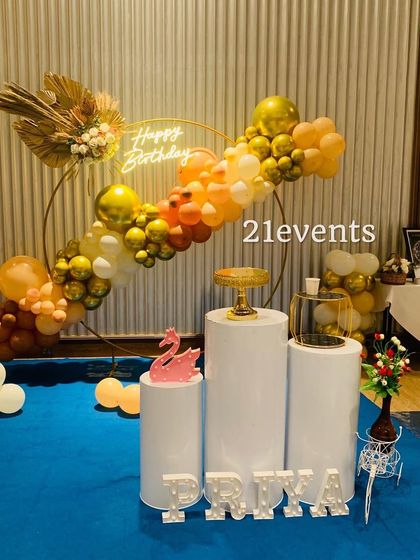 An elegant and modern birthday setup with a boho-chic vibe. The asymmetrical balloon arch on a gold ring features dried palm leaves and a warm color palette.