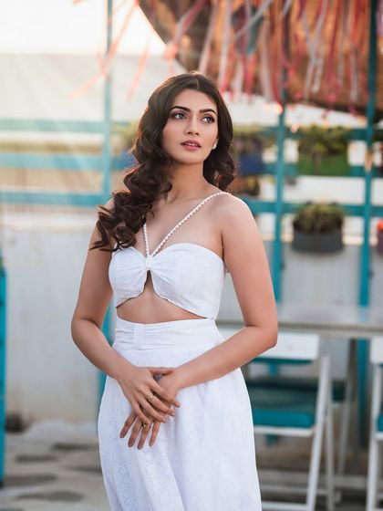 A half-body shot from a rooftop fashion shoot. The composition focuses on the details of the white two-piece outfit and the model's relaxed yet chic demeanor.